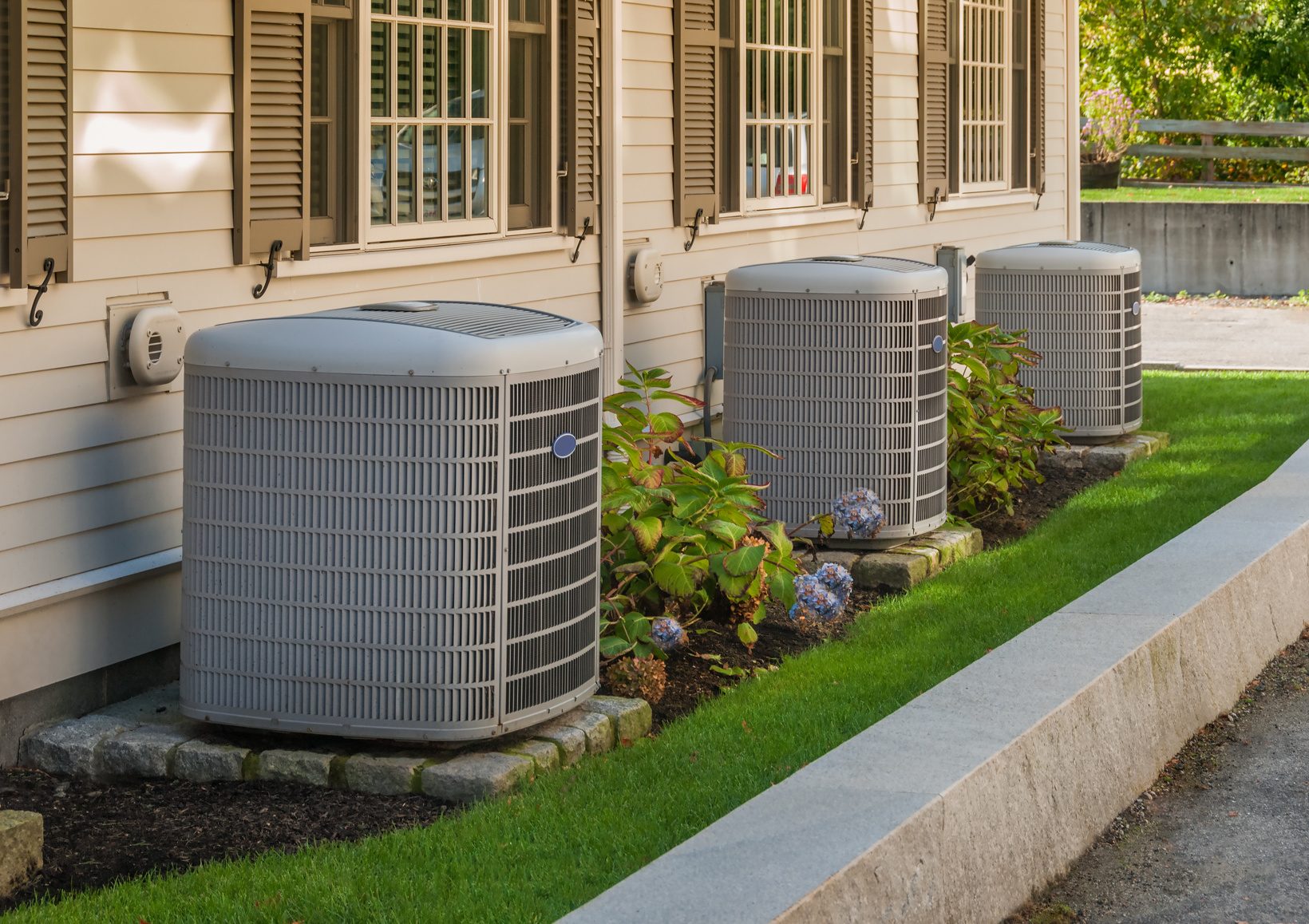 Three outdoor air conditioning condensers beside a home